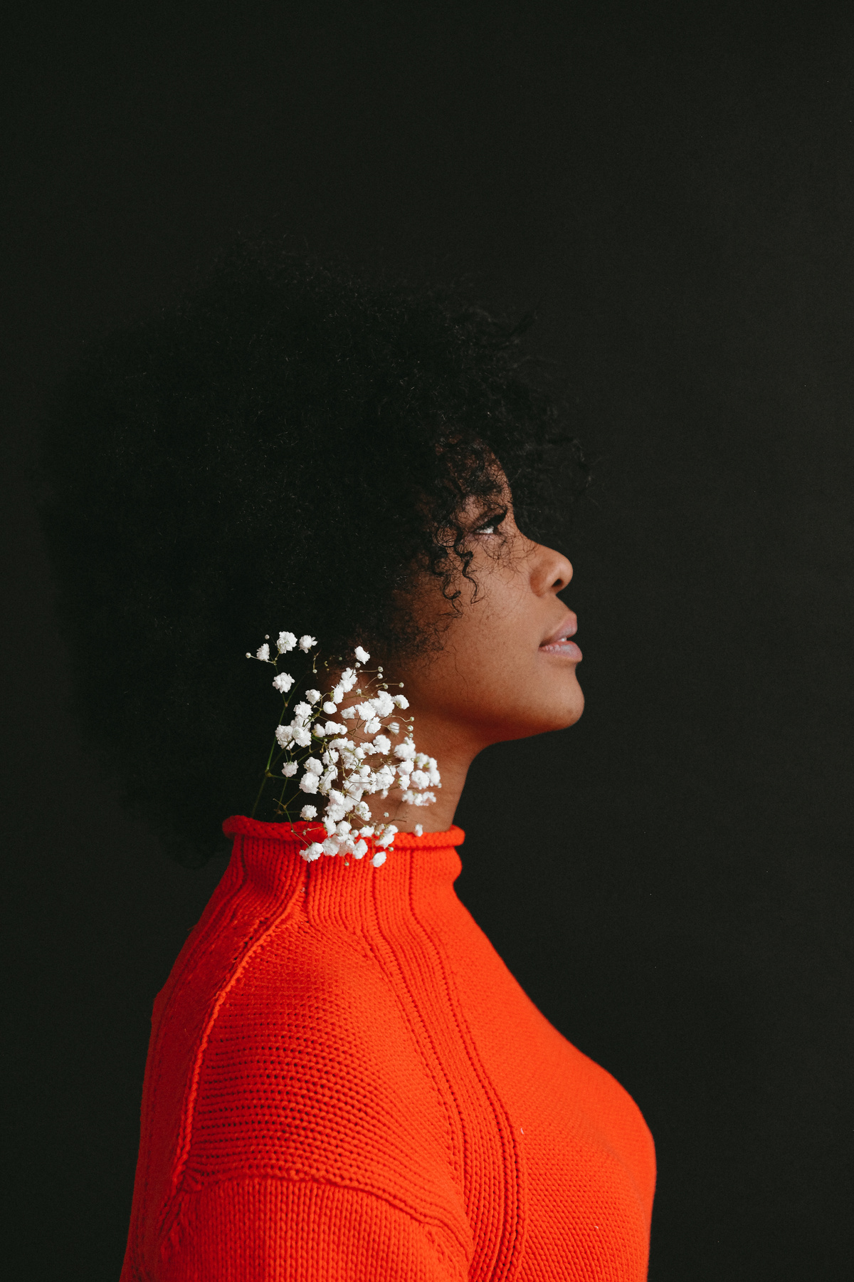 Woman in Red Turtleneck Shirt With White Flowers on Ear